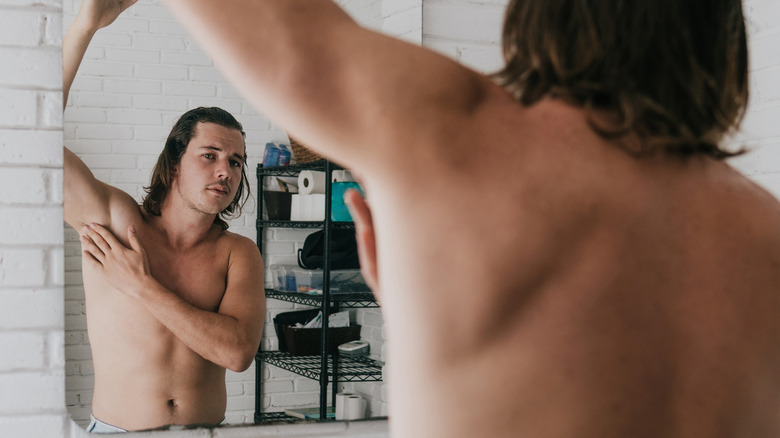 man applying deodorant while looking in mirror at self
