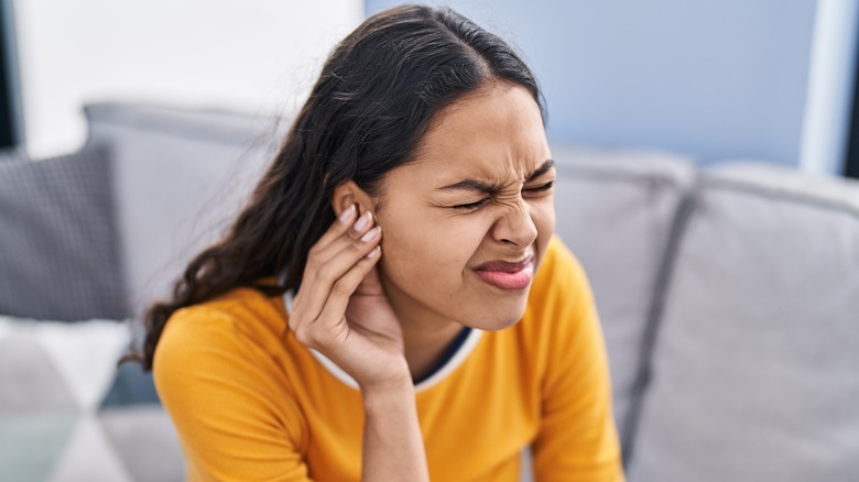 Wincing woman touching ear in pain