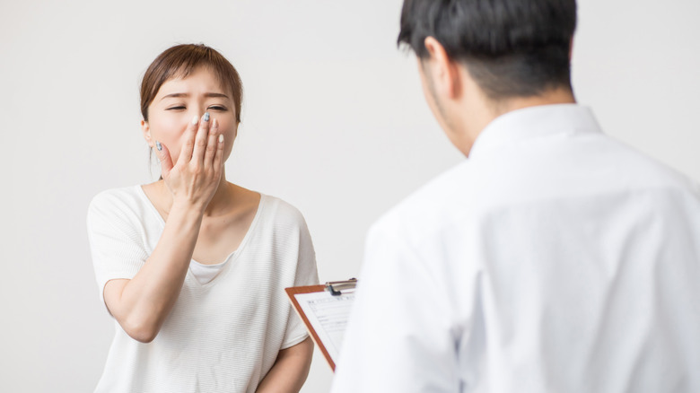 Woman covering her mouth while yawning and receiving consultation from doctor