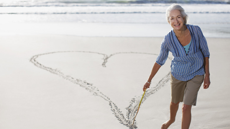 older woman drawing a heart in the sand