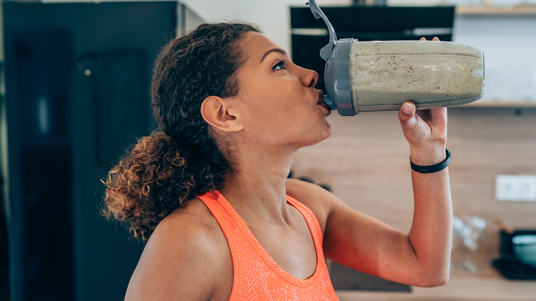 woman wearing workout clothes drinking a smoothie 