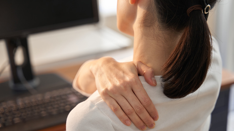 Woman grasping shoulder at desk