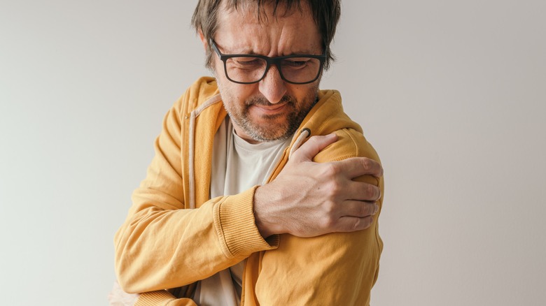 Grimacing man holding left shoulder