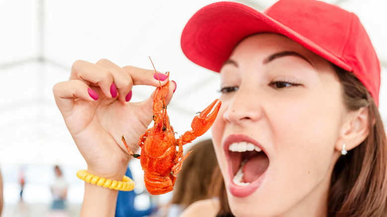 woman holding a crawfish up to mouth