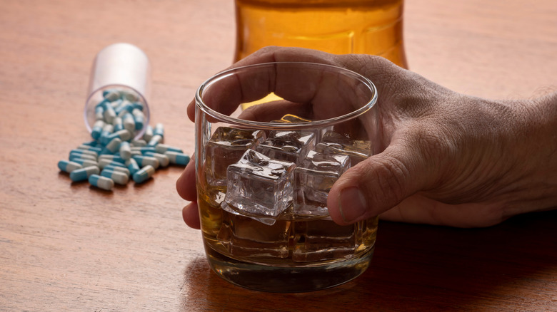 Hand holding whiskey glass with pills on table