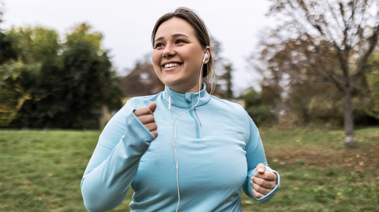 A happy woman running outdoors while wearing earbuds