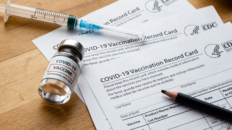 Needles, a vaccine vial, and vaccination cards on a desk