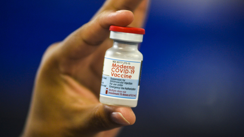 A hand holds up a vial of Moderna vaccine