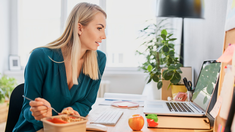 Woman looking at her laptop while eating