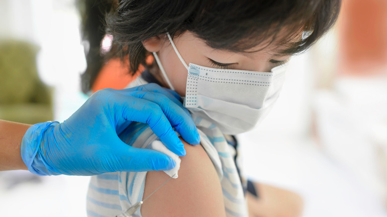 Young masked child receiving vaccine in upper arm