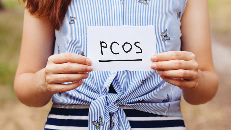 Woman holding up a piece of paper that says "PCOS"