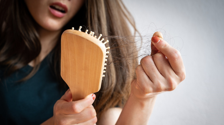 Woman with long hair looking distressed at the hair in her hairbrush