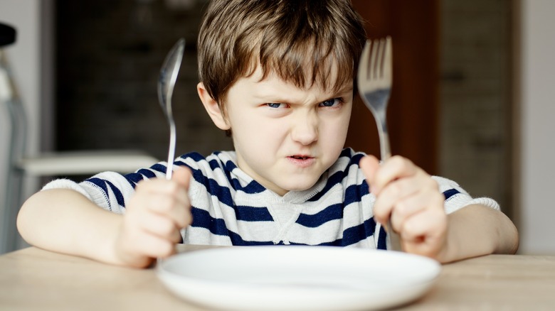 Angry hungry child holding silverware