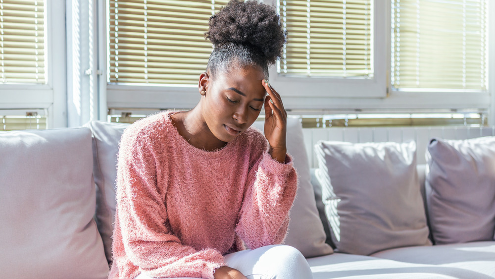 Young Black woman sitting, eyes closed and touching forehead