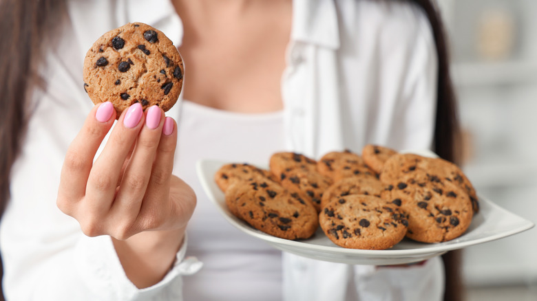 A woman holding a single cookie and a plate of cookies