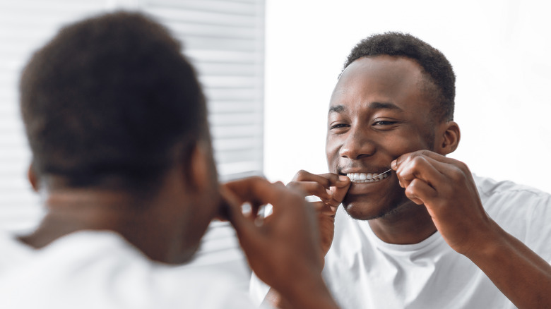 man flossing teeth in mirror