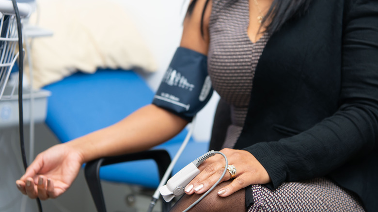 Woman sits in doctor's office wearing blood pressure cuff and pulse oximiter