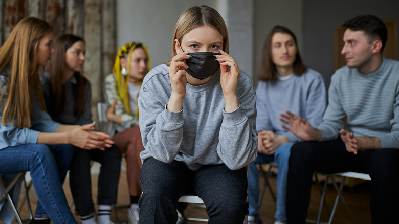 Masked woman sitting among unmasked people