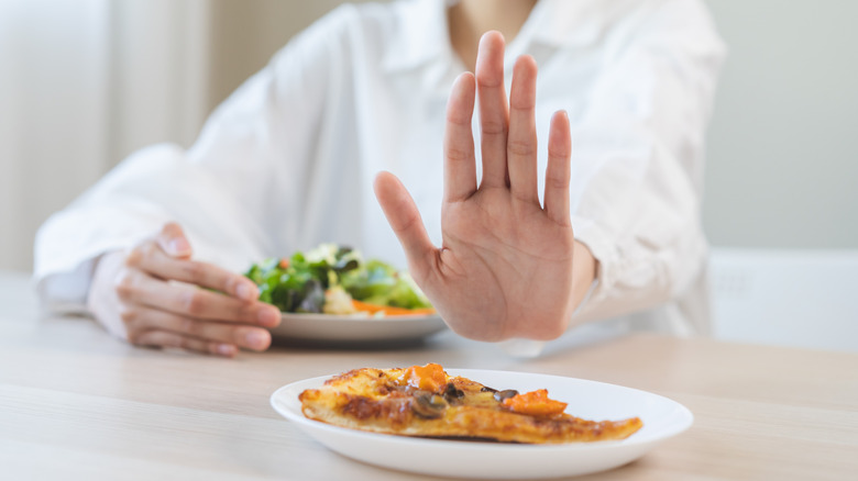 A woman's hand pushing away a slice of pizza