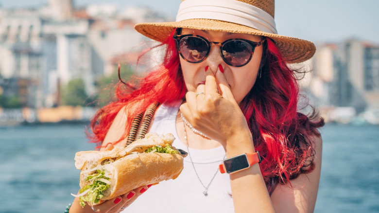 A woman holding her nose while holding a sandwich