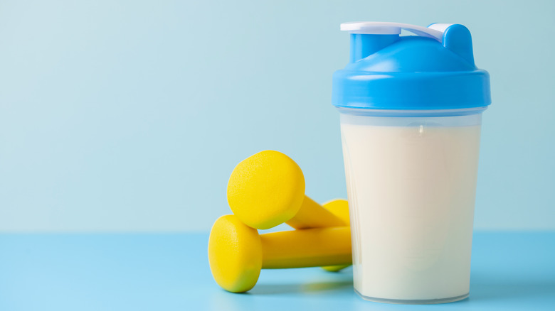 A protein shake next to a pair of dumbbells