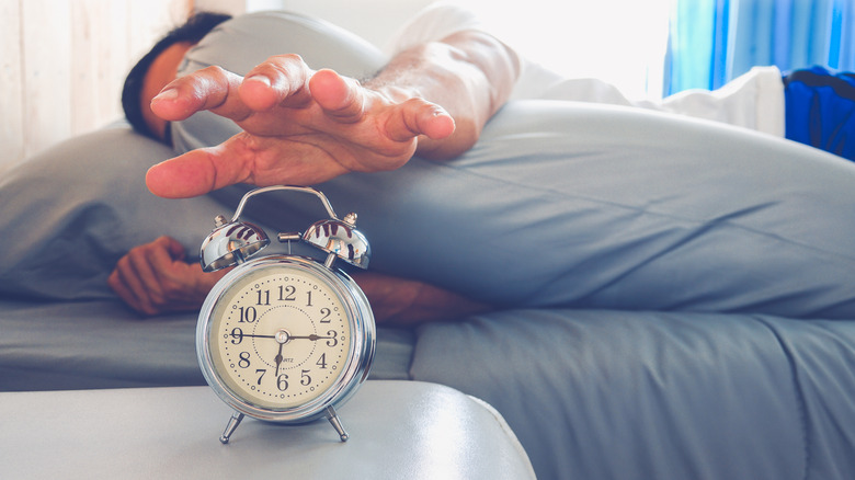 A man presses the snooze button on an alarm clock