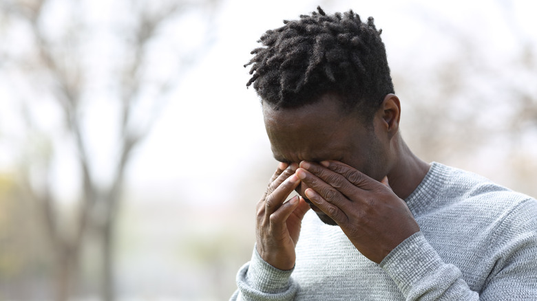 A man standing outside rubbing his eyes