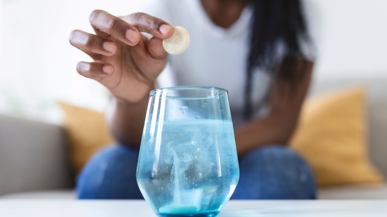 woman dropping antacid in glass of water