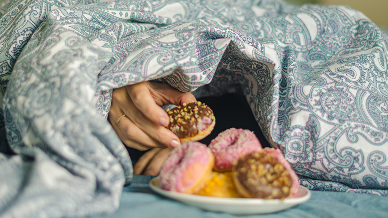 woman's hand reaching for food from under bed covers