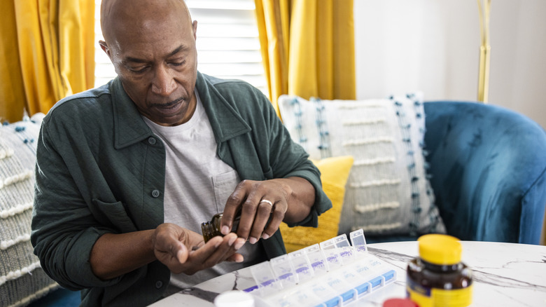 mature man seated at table taking vitamins at home