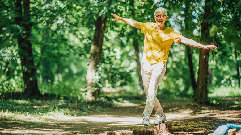 older woman balancing on a tree trunk