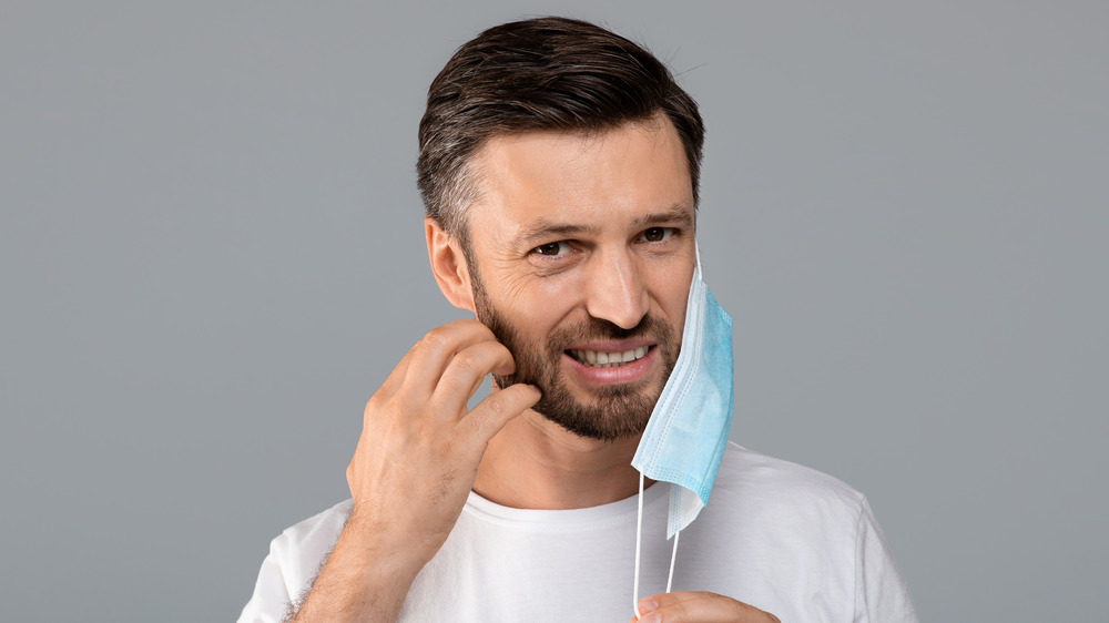 Man with beard taking off mask