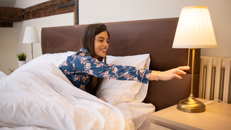 A smiling woman turns off the light before going to bed