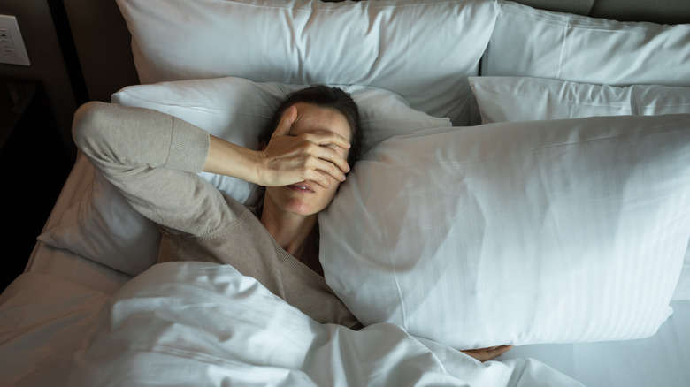 A woman in bed with her hand over her eyes as she suffers from insomnia