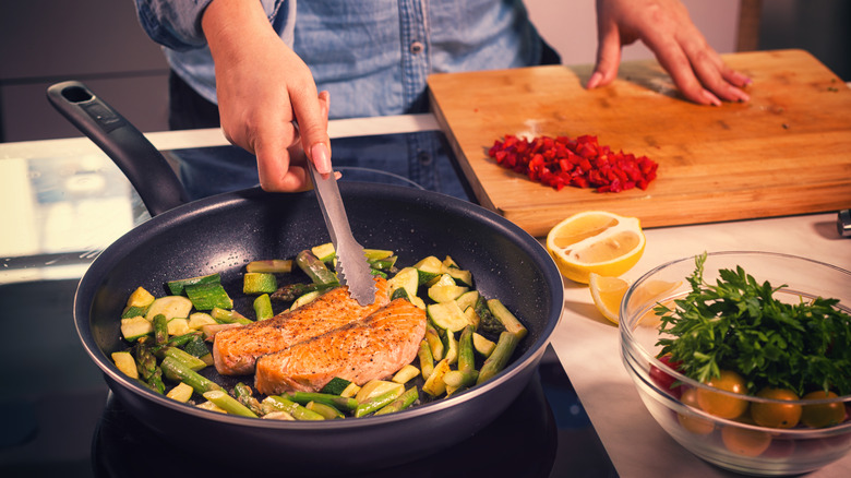 Woman cooking fish with vegetables