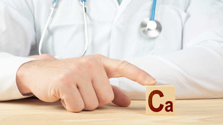 Close up of a doctor's hand using one finger to touch a block with the letters "Ca" on it