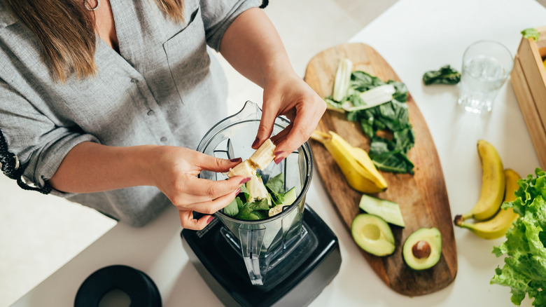 Woman using blender on vegetables and fruits