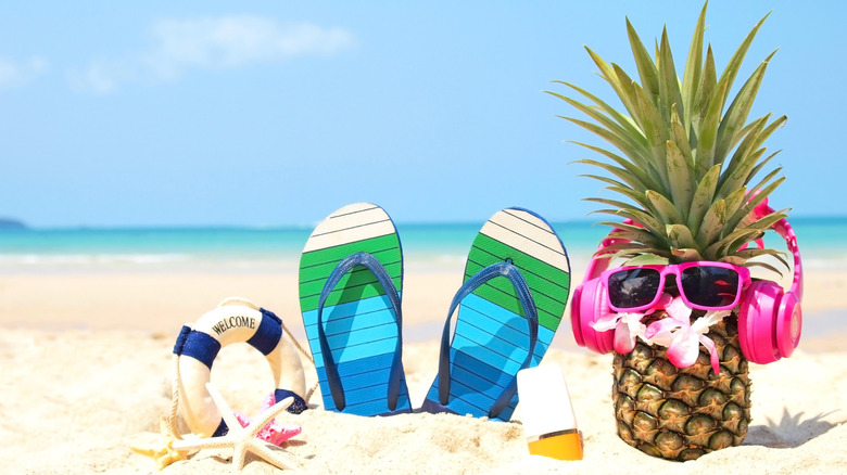a pair of sandals sticking out in the sand with a pineapple