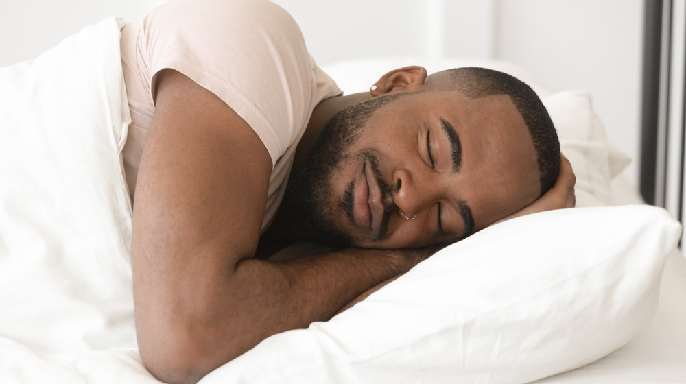 Person asleep in bed with hands tucked under head on pillow