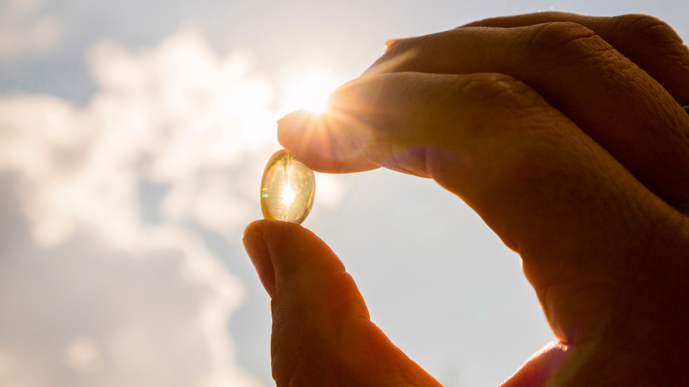 Fingers holding vitamin D supplement up to the sun