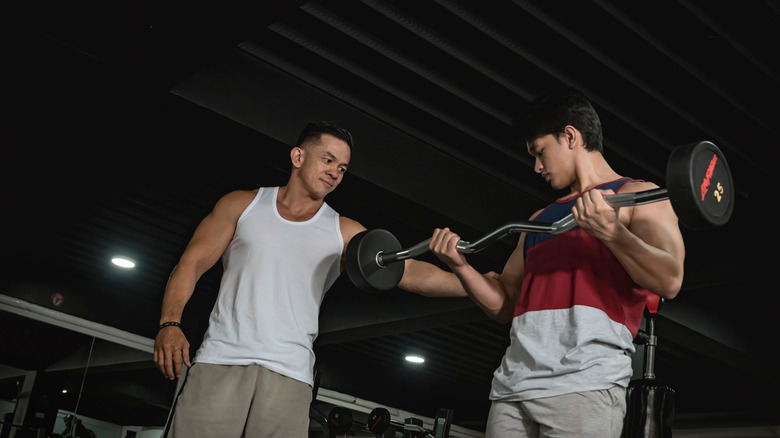 Trainer helping man do bicep curls in gym